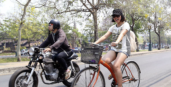 In this March 30, 2014 photo, a Chinese tourist rides on a bicycle during a tour in downtown Chiang Mai province, northern Thailand. The bucolic, once laid-back, campus of one of Thailand’s top universities seems to be under a security clampdown ... <br srcset=